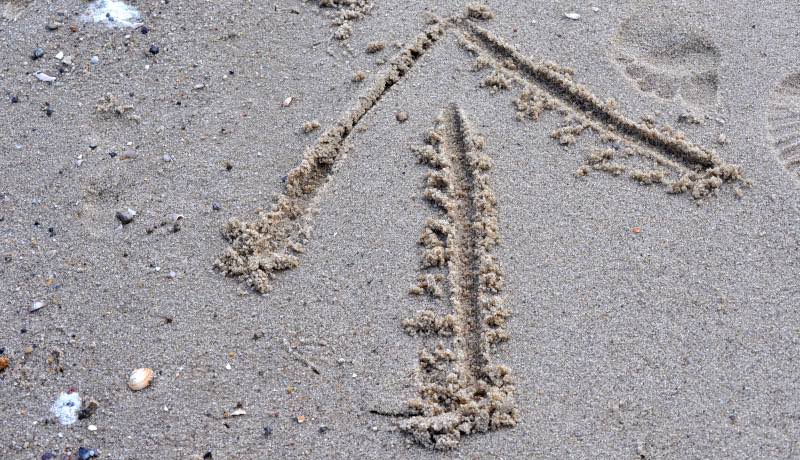 een naar boven gerichte pijl getekend met een stok in het zand van een strand